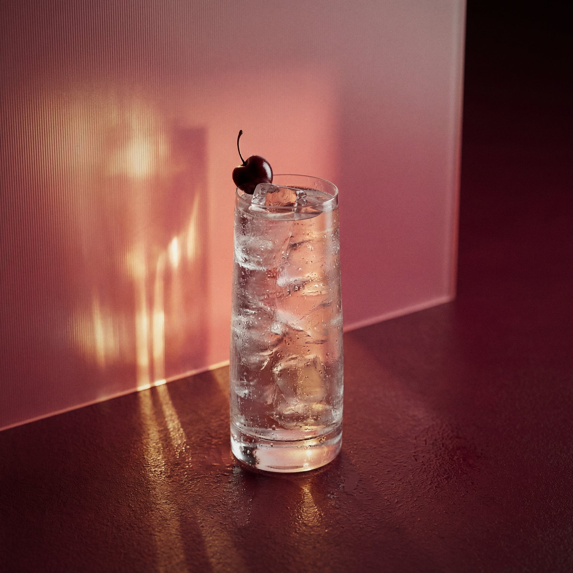 kirsche easy mix cocktail with a cherry in a highball glass with kirsche liqueur  on a dark surface with pinkish-brown background