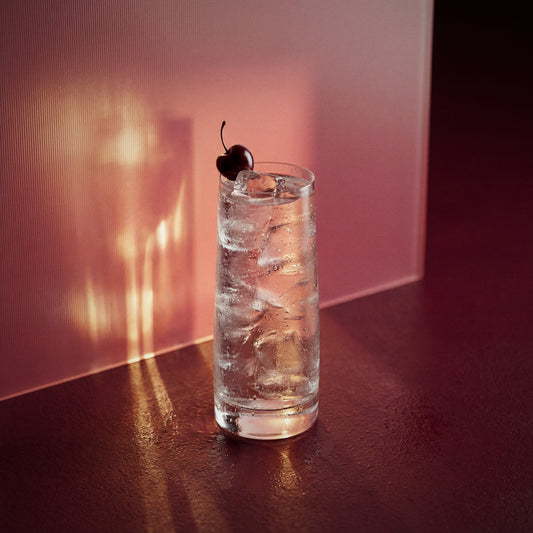 kirsche easy mix cocktail with a cherry in a highball glass with kirsche liqueur  on a dark surface with pinkish-brown background