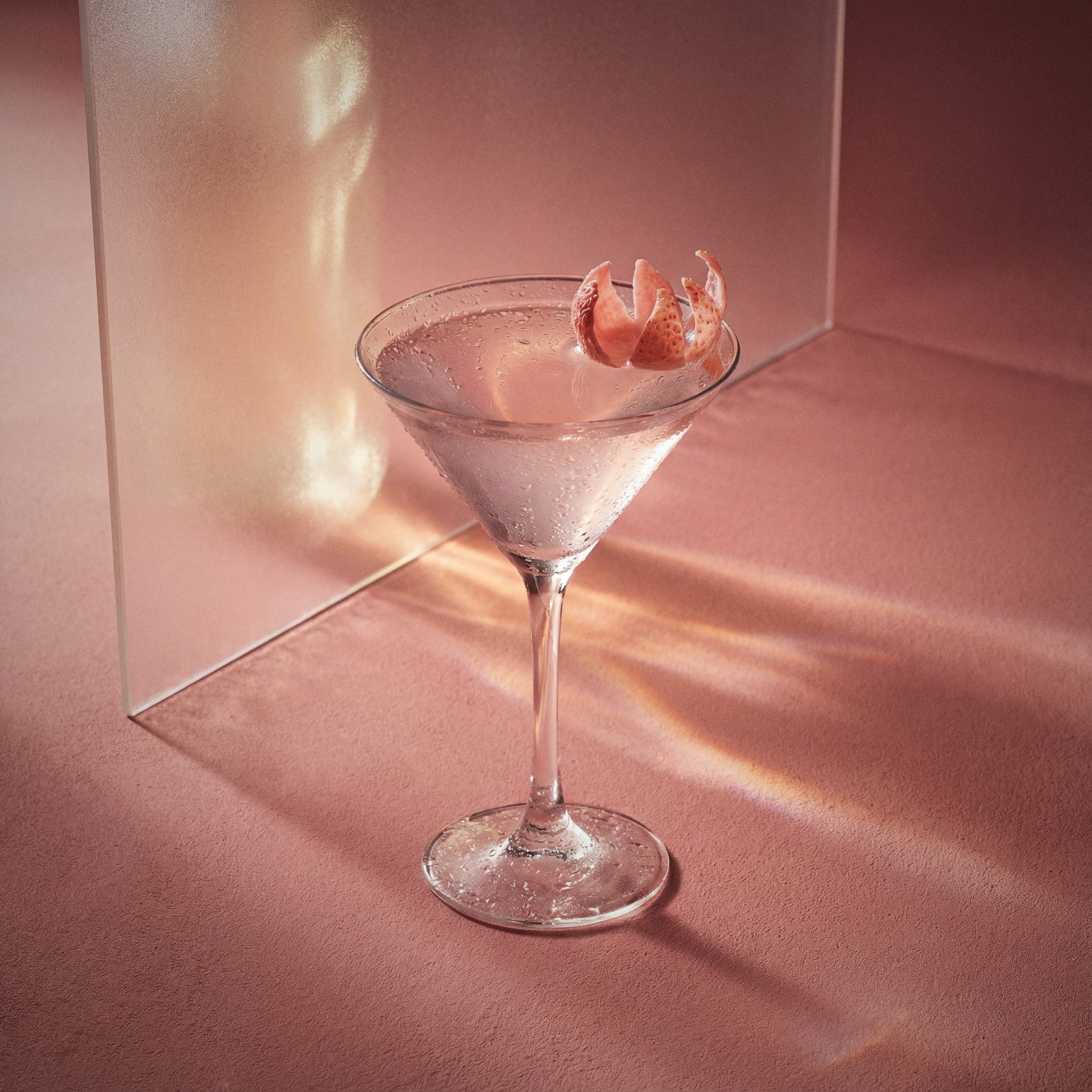 lychee martini cocktail in a martini glass with a lychee garnish on a pink background made with lychee liqueur and vodka