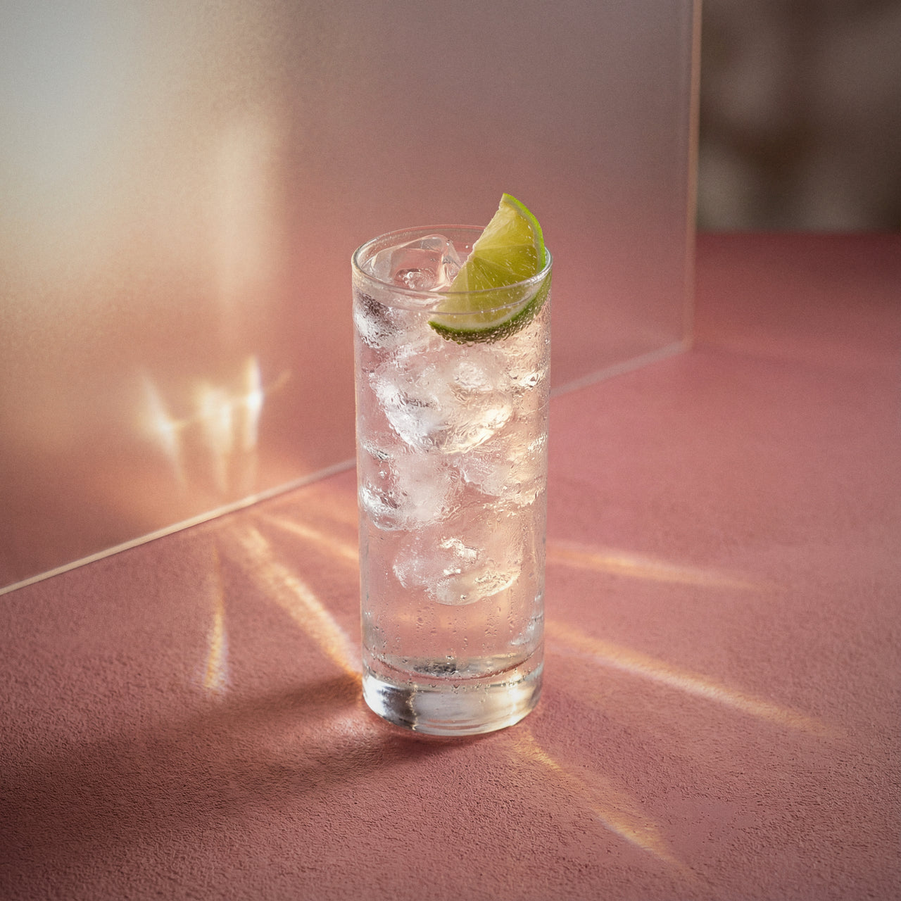 lychee rickey cocktail with lychee liqueur in a highball glass with a lime wedge on a pink background