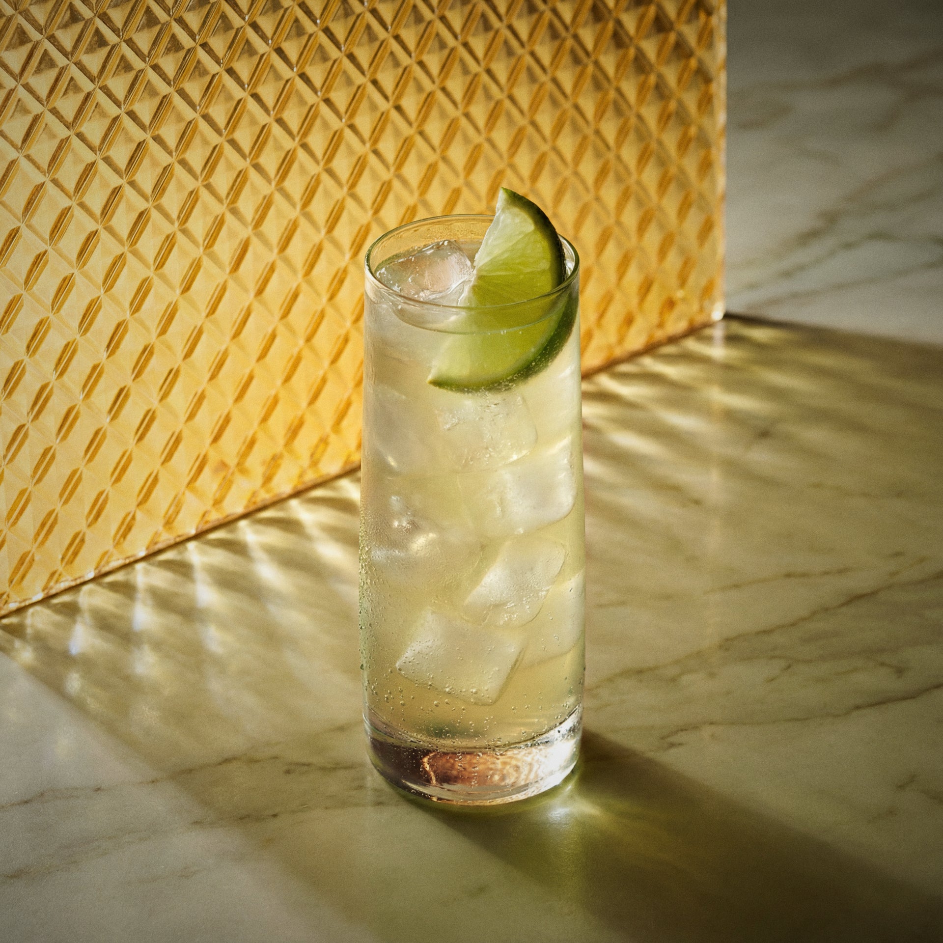mango easy mix cocktail with mango liqueur in a highball glass and with a lime wedge on a textured yellow surface