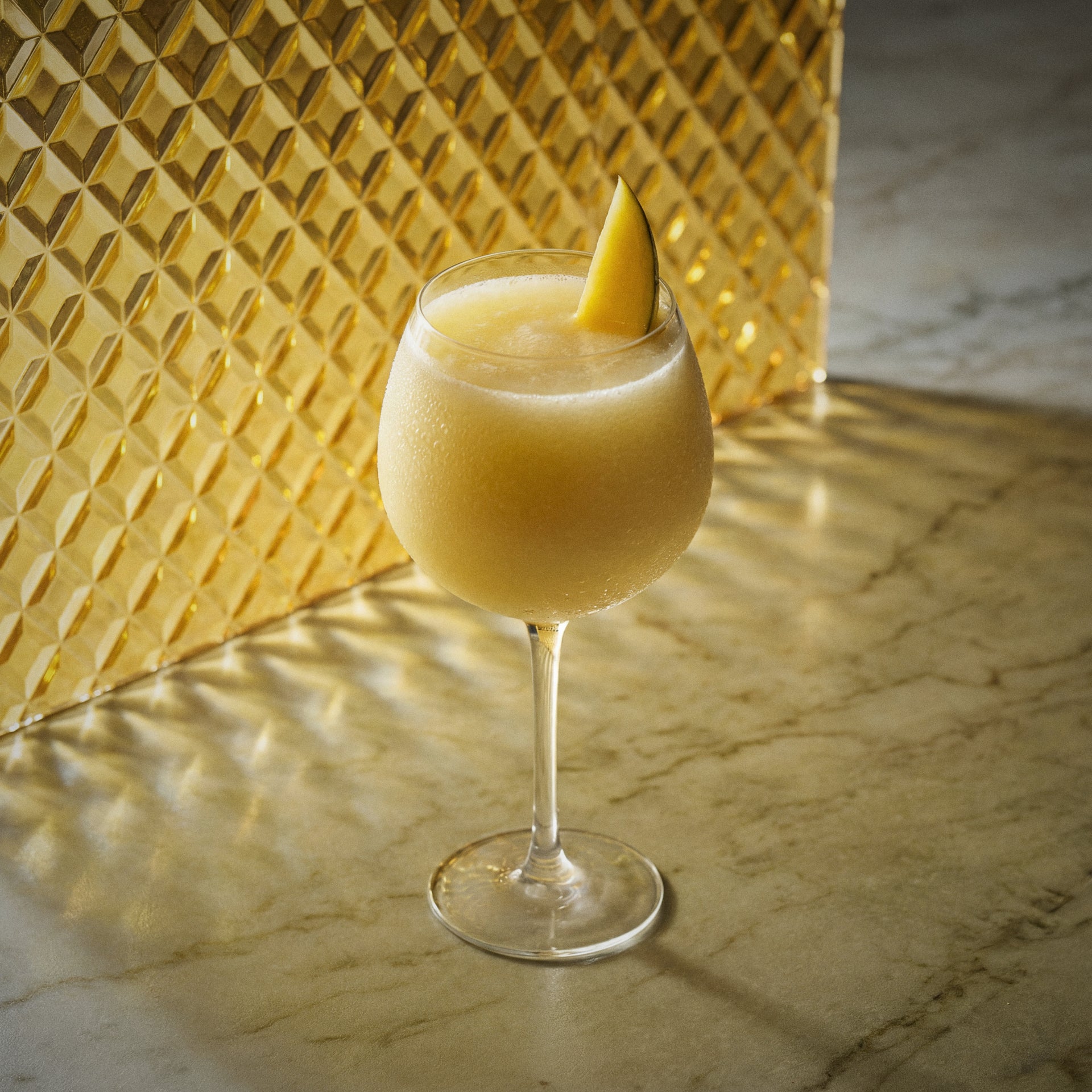 mango lassi cocktail with mango liqueur in a wine glass and mango slice on a textured yellow surface