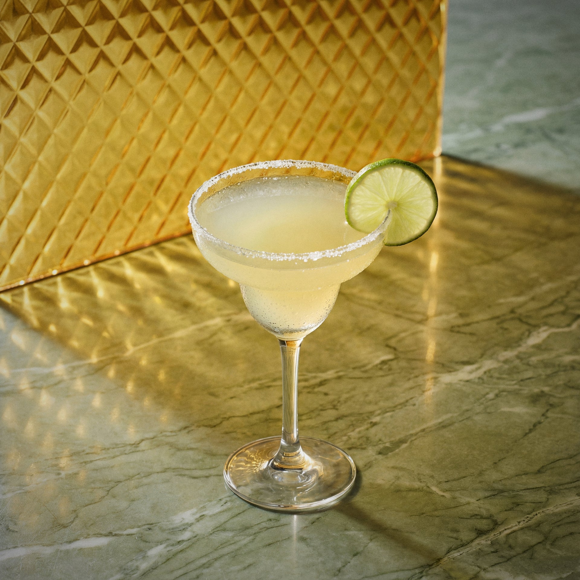mango margarita cocktail with mango liqueur in a margarita glass with a lime wedge on a marble surface