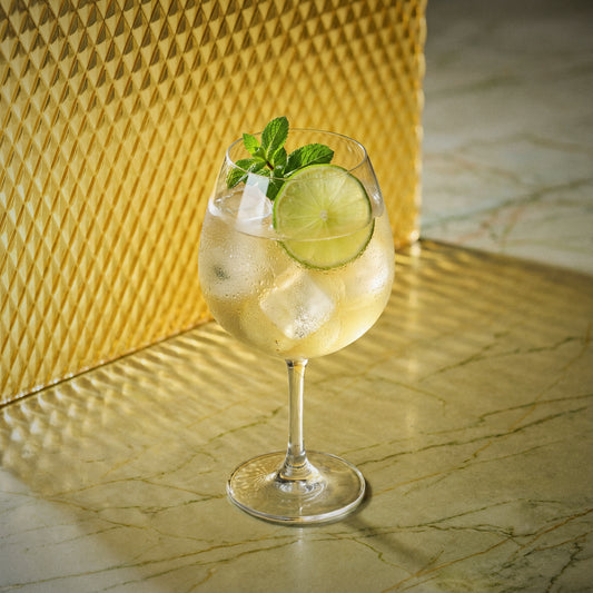 mango spritz cocktail with mango liqueur in a large wine glass garnished with a lime wheel and mint sprig on a yellow surface