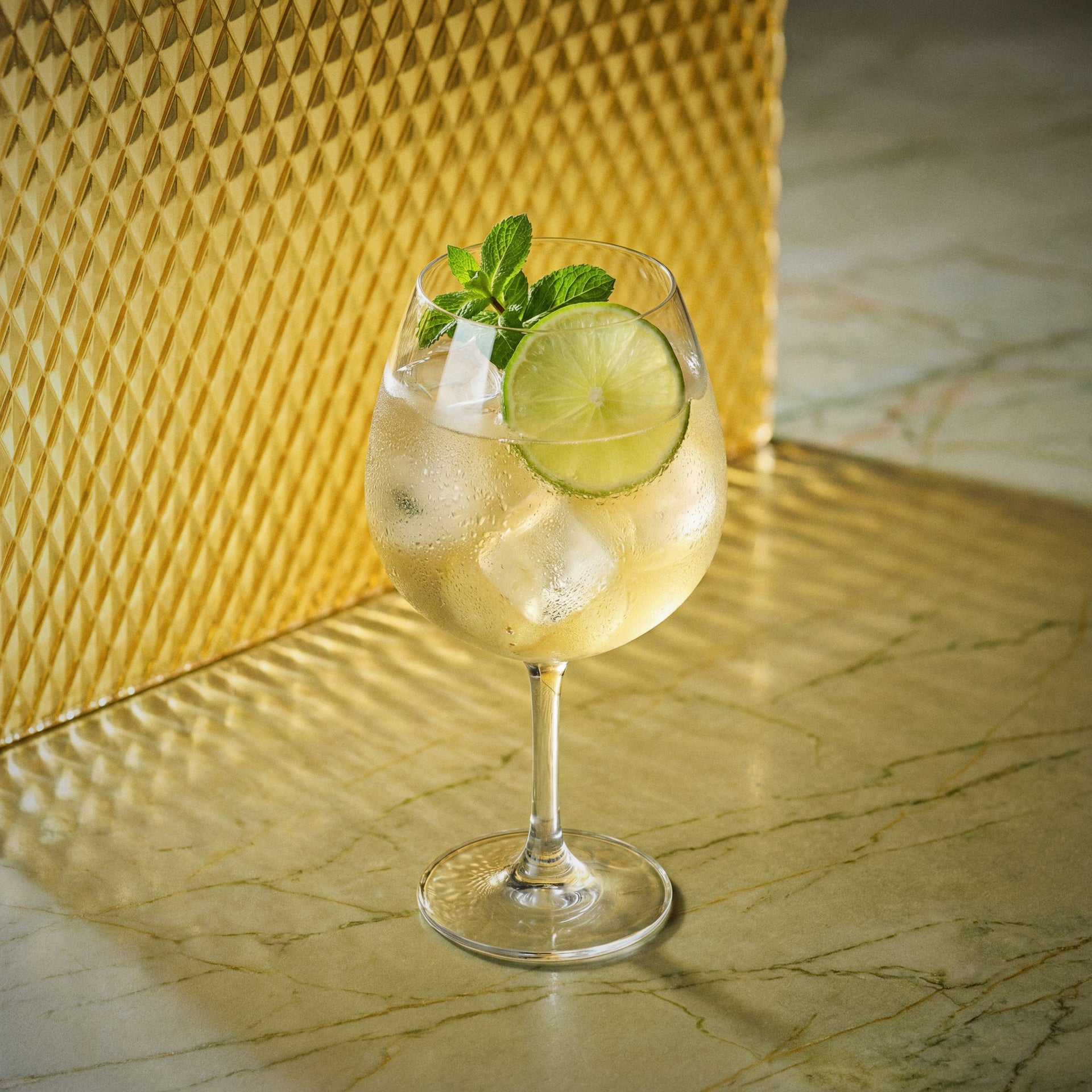 mango spritz cocktail with mango liqueur in a large wine glass garnished with a lime wheel and mint sprig on a yellow surface