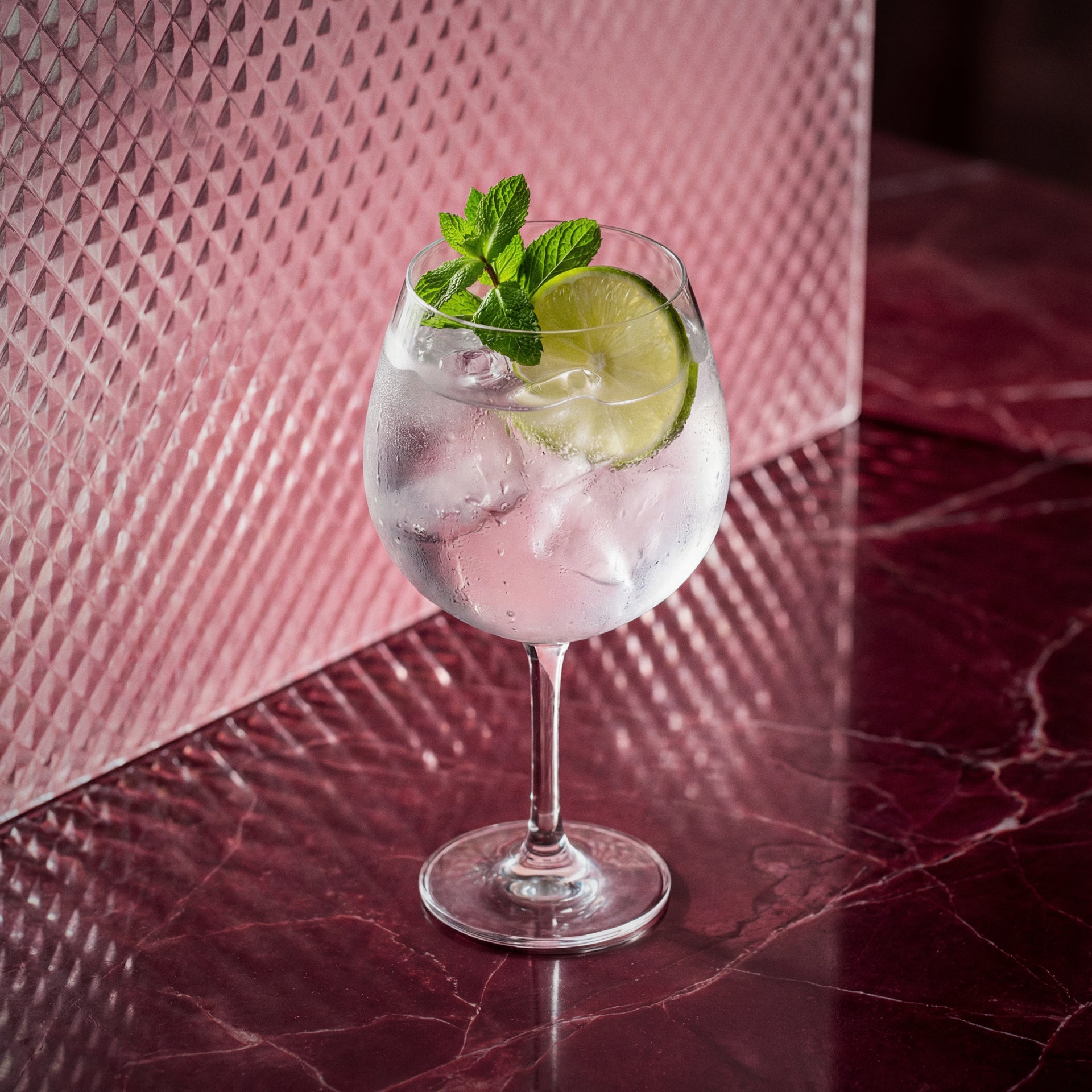 Maraschino spritz cocktail with Maraschino liqueur and with lime and mint in a wine glass on a pink marble surface.