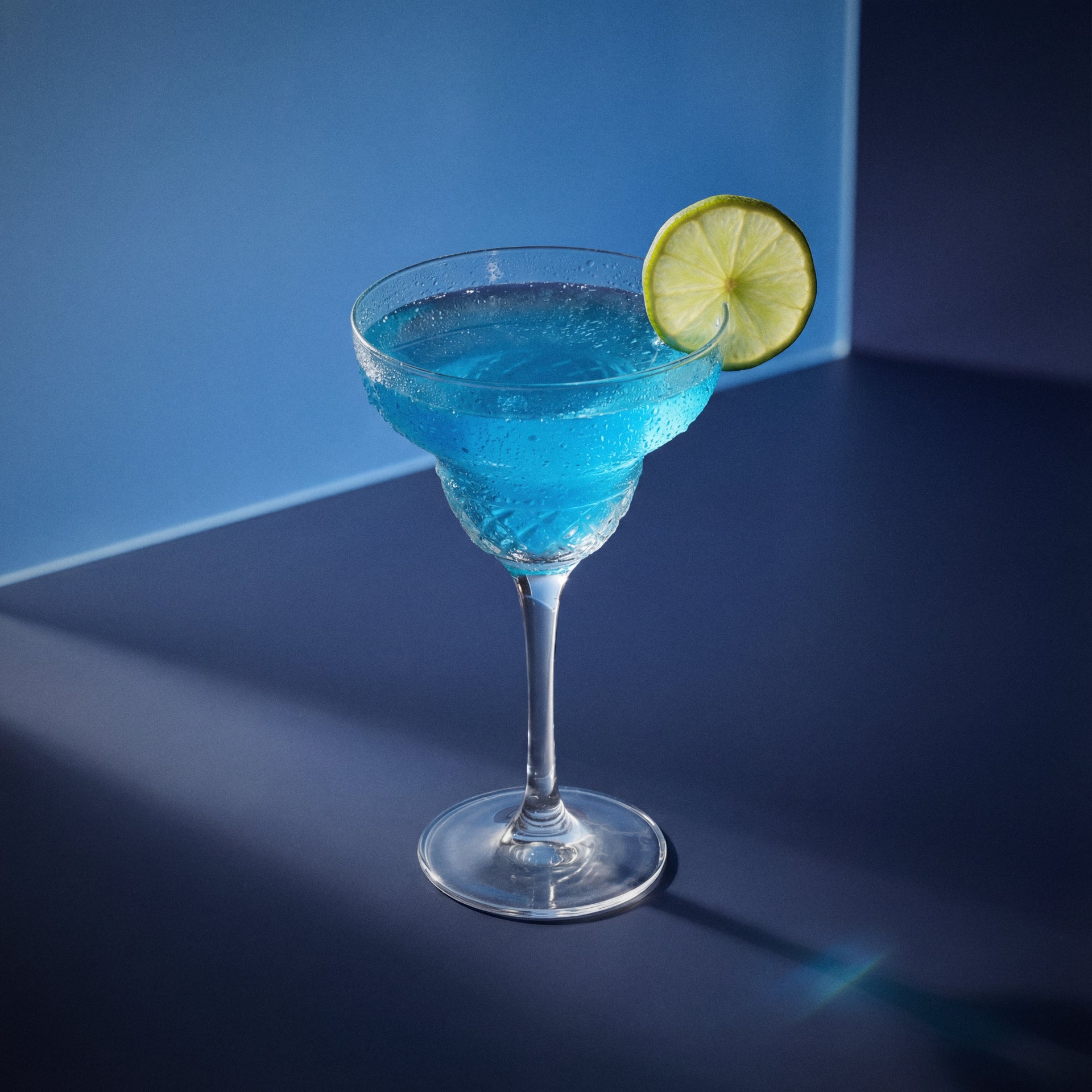 margarita azul cocktail with blue curacao liqueur in a martini glass with a lime wedge on a blue background
