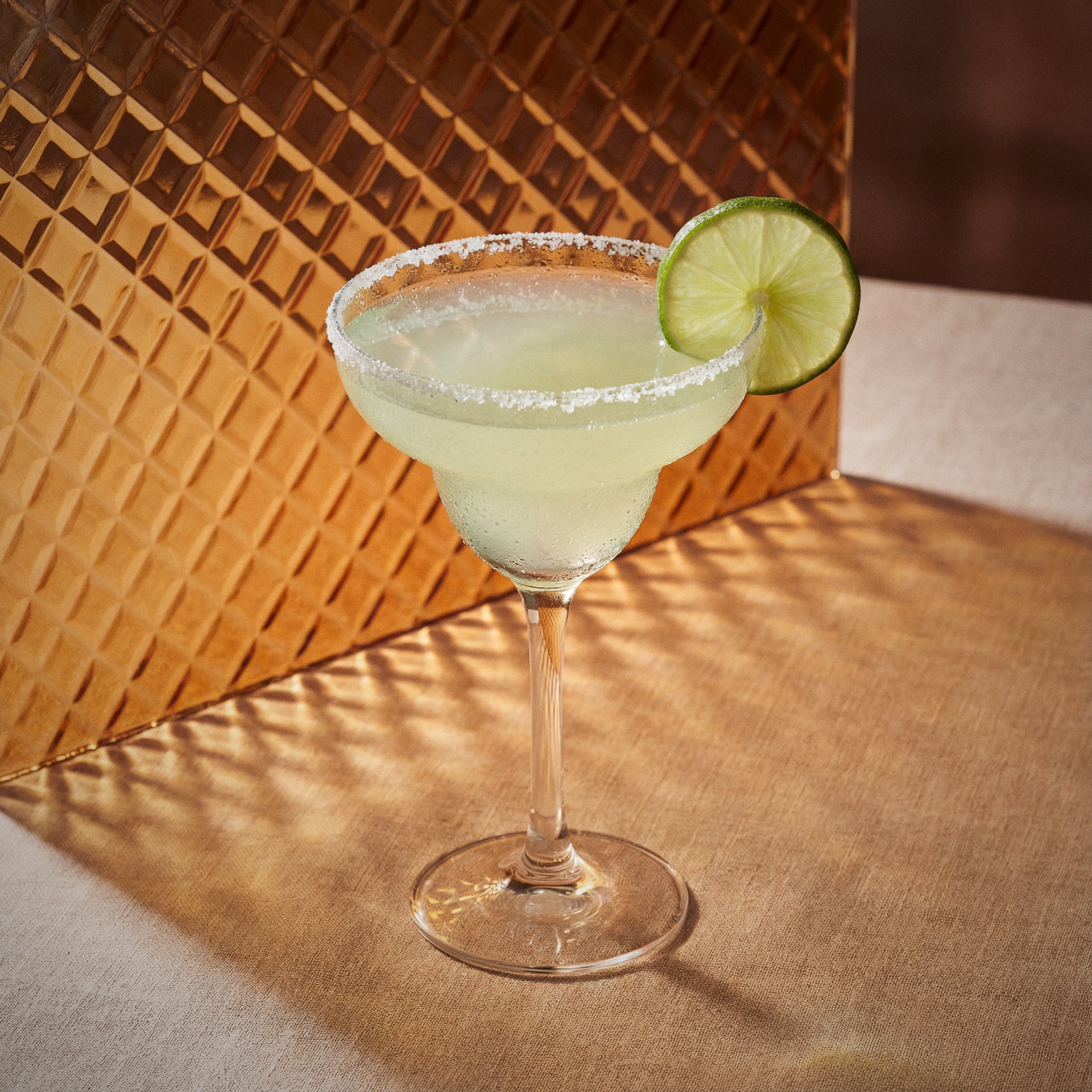 margarita cocktail with triple sec liqueur in a margarita glass with a lime wheel on a orange textured surface