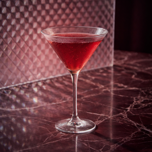 martinez cocktail in a martini glass with maraschino liqueur an genever on a marbled surface with a patterned wall in the background