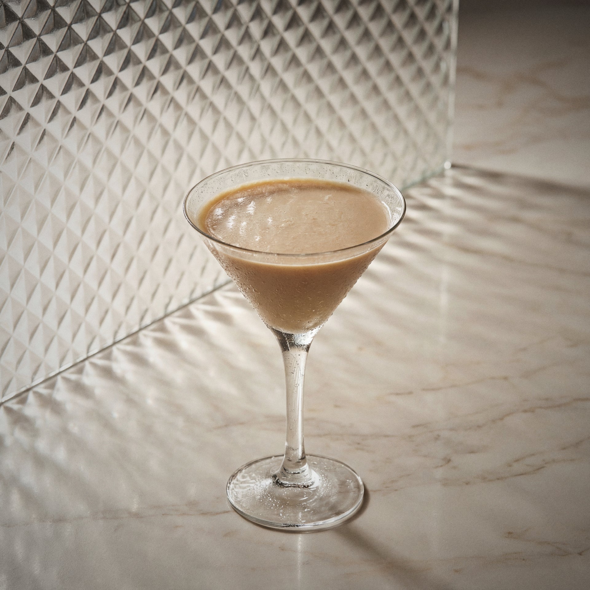 mud slide cocktail made with natural yoghurt liqueur, coffee liqueur, cacao brown liqueur, in a martini glass and on a glass surface
