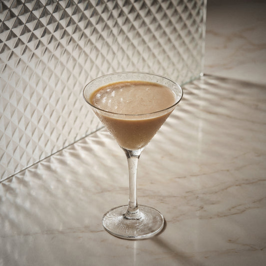 mud slide cocktail made with natural yoghurt liqueur, coffee liqueur, cacao brown liqueur, in a martini glass and on a glass surface