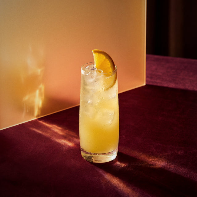 orange collins cocktail with dry orange liqueur and genever and with ice and lemon wedge on a dark surface