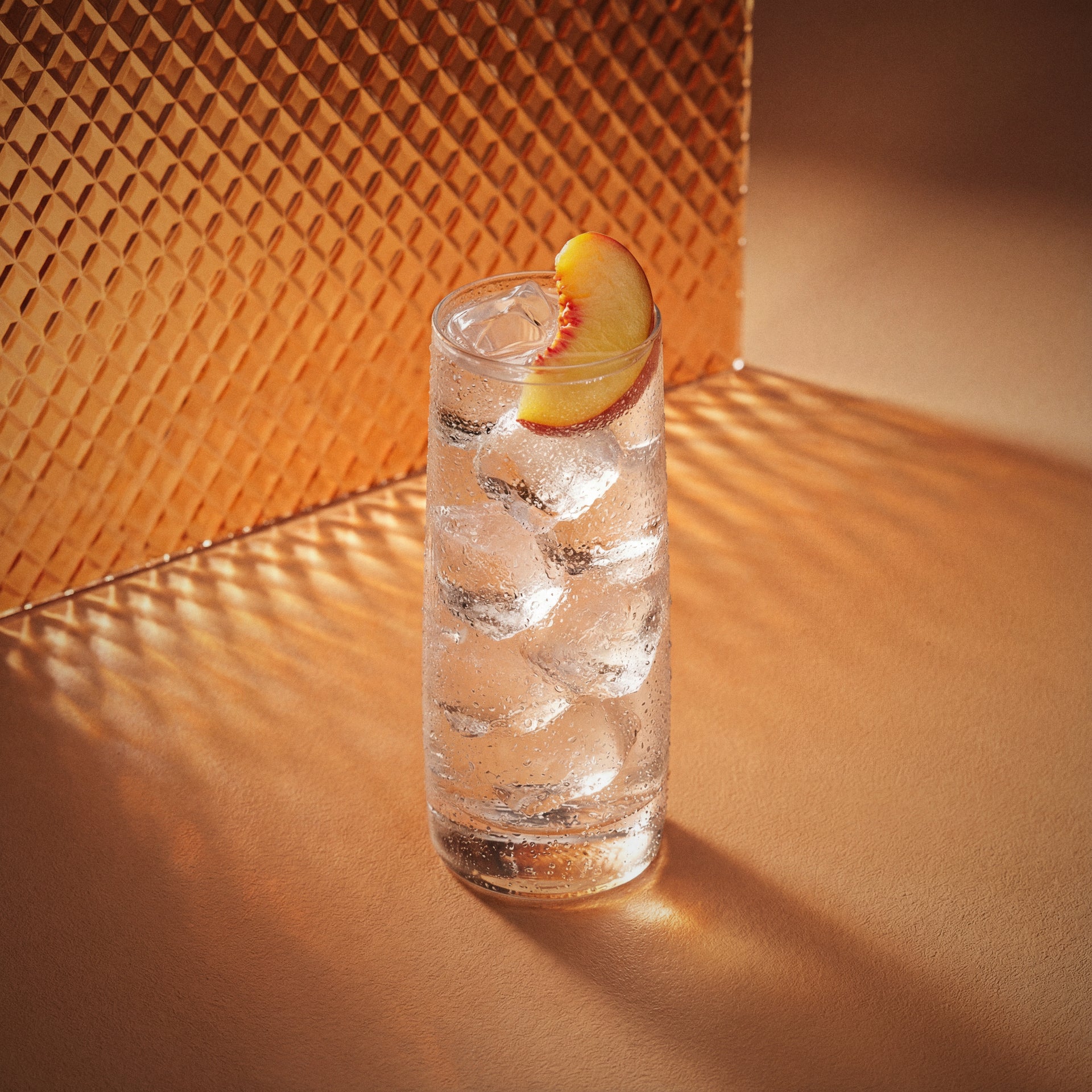 peach easy drink cocktail in a highball glass with ice and a slice of fruit on a textured surface