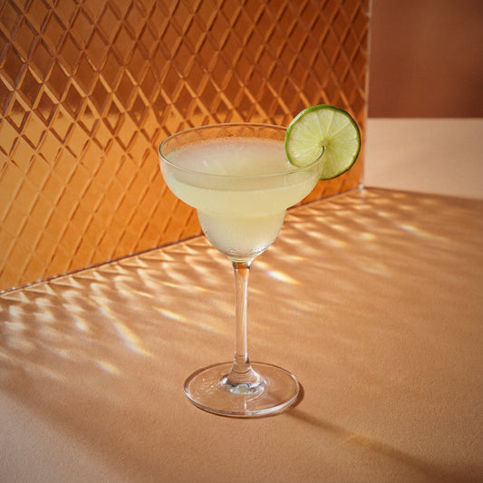 peach margarita cocktail with peach liqueur and triple sec liqueur in a margarita glass with a lime wheel on a textured wall background