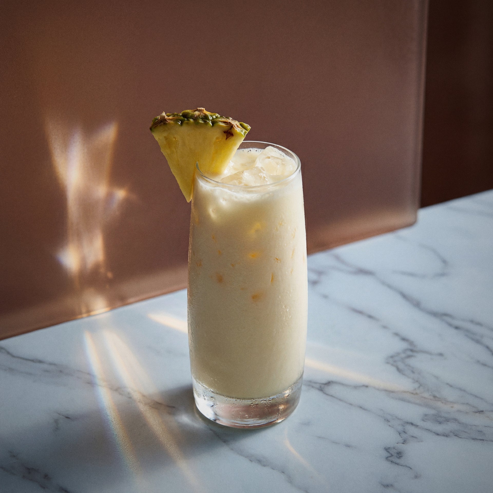 pina colada cocktail with coconut liqueur with a slice of pineapple in a highball glass on a marble surface