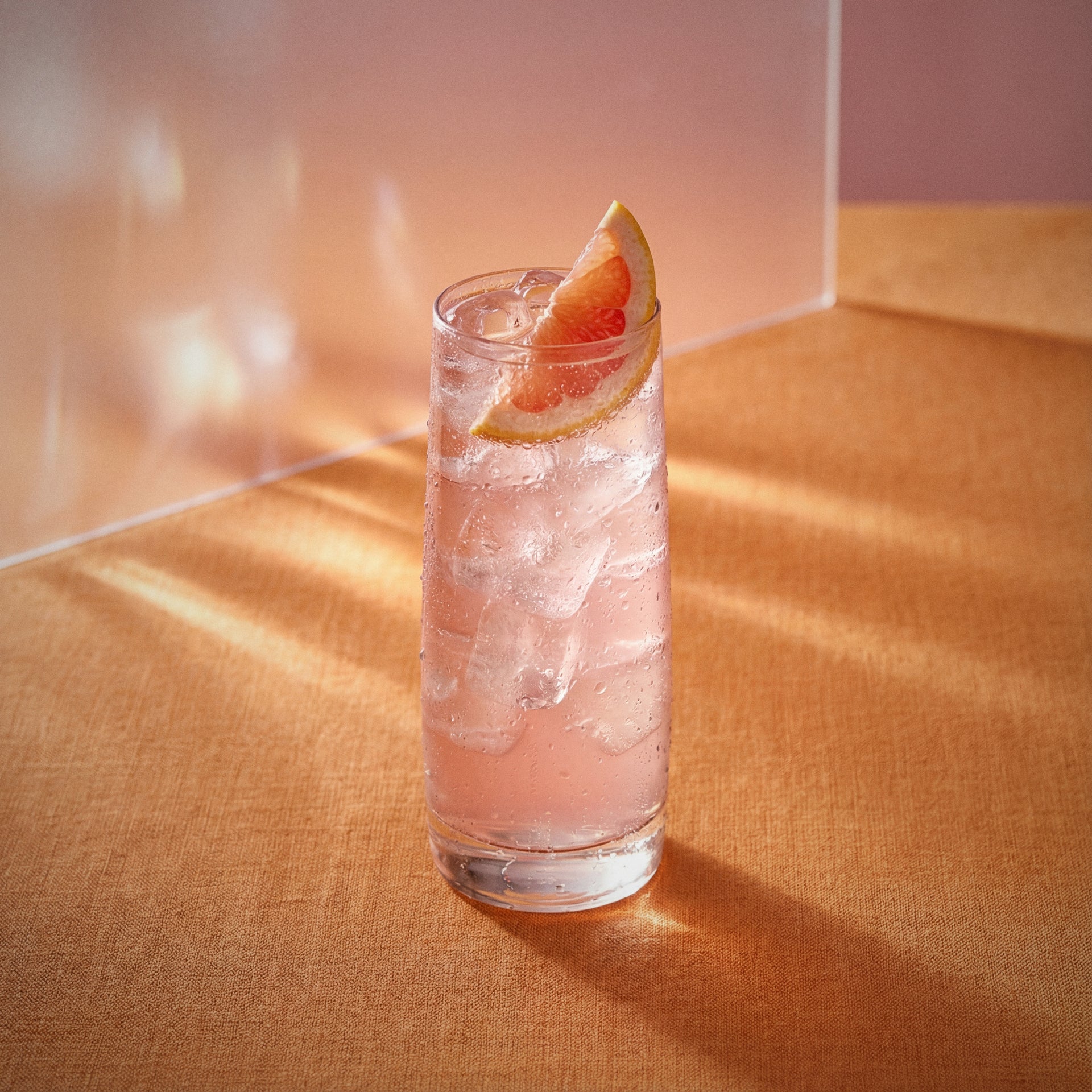 pink grapefruit easy mix cocktail with ice and a grapefruit wedge made with pink grapefruit liqueur on a textured surface