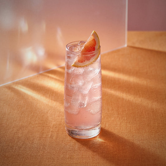 pink grapefruit easy mix cocktail with ice and a grapefruit wedge made with pink grapefruit liqueur on a textured surface