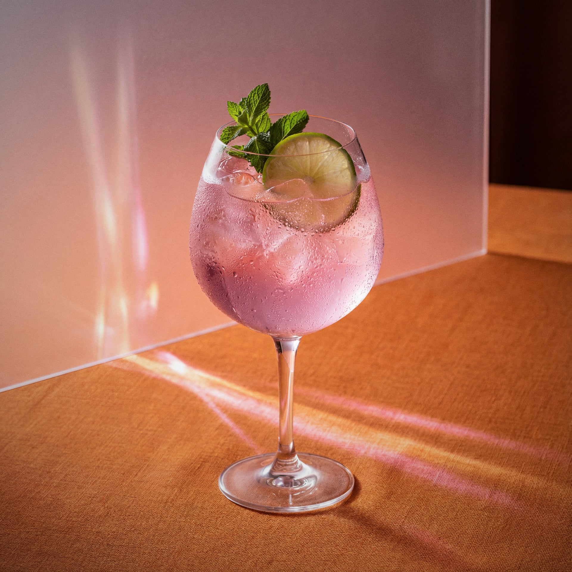 Pink grapefruit spritz cocktail with pink grapefruit liqueur and lime and mint in a wine glass on a warm-toned surface