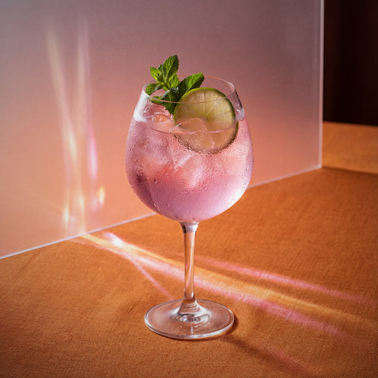 Pink grapefruit spritz cocktail with pink grapefruit liqueur and lime and mint in a wine glass on a warm-toned surface