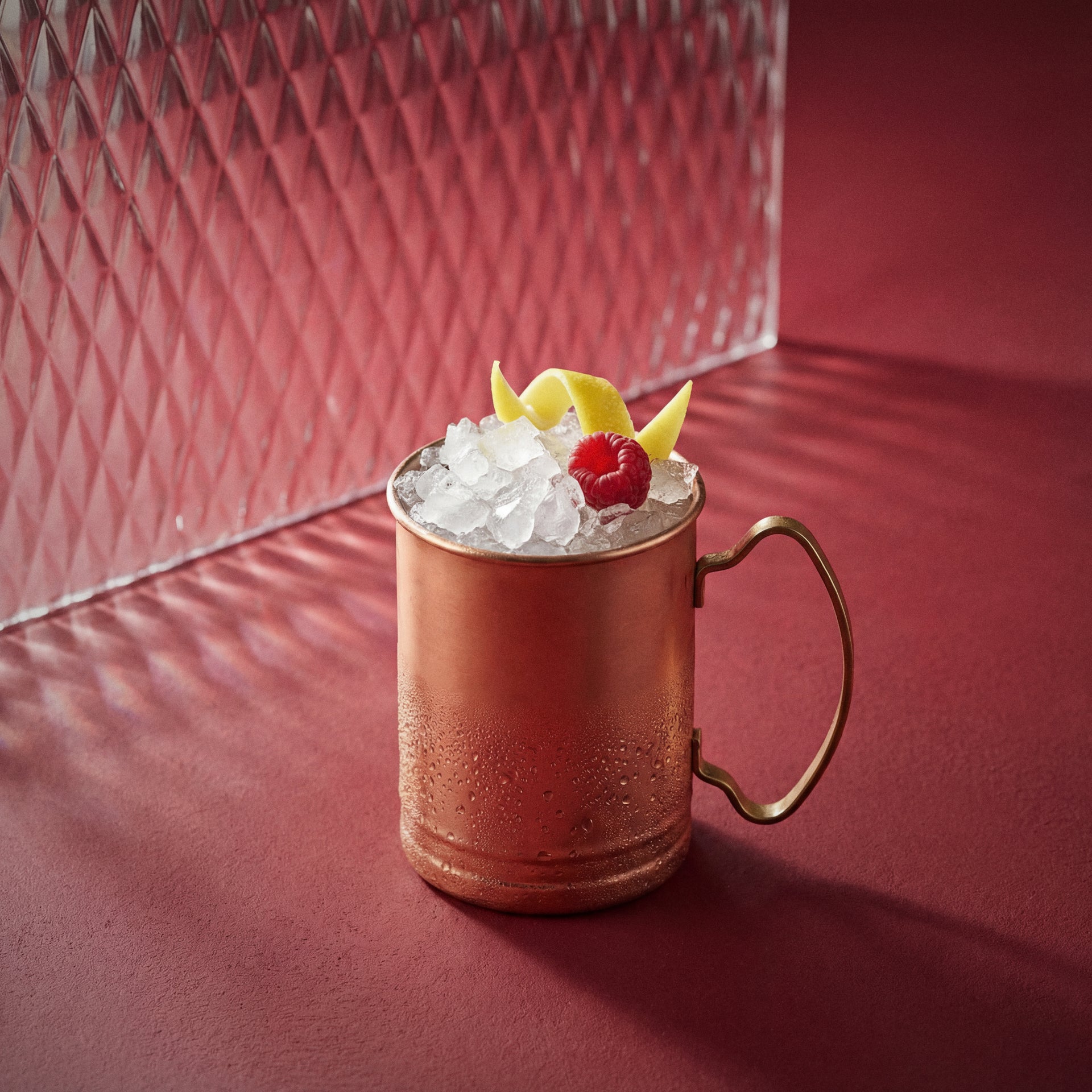 raspberry mule cocktail with raspberry liqueur in a copper mug on a red surface
