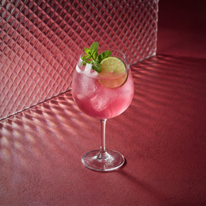 raspberry spritz cocktail with lime and mint in a coppa glass on a red textured surface 