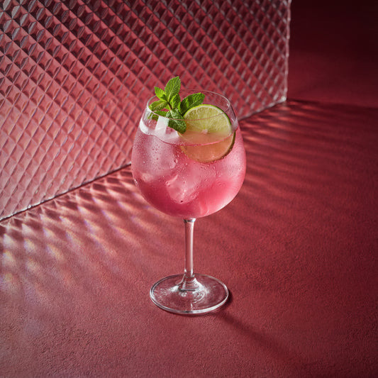 raspberry spritz cocktail with lime and mint in a coppa glass on a red textured surface 