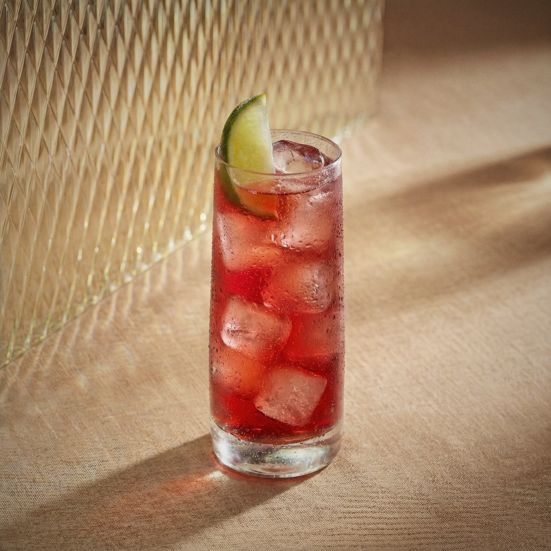 Red headed ginger cocktail with ginger liqueur and genever and a lime wedge in a highball glass on a textured surface