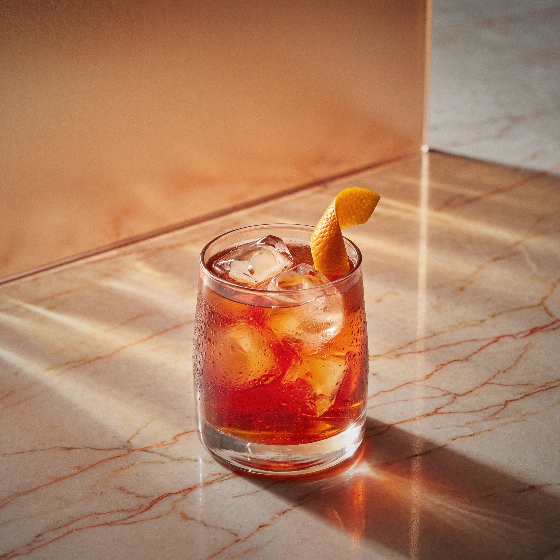 Red light negroni cocktail with bols genever in a rocks glass with an orange twist on a marble surface