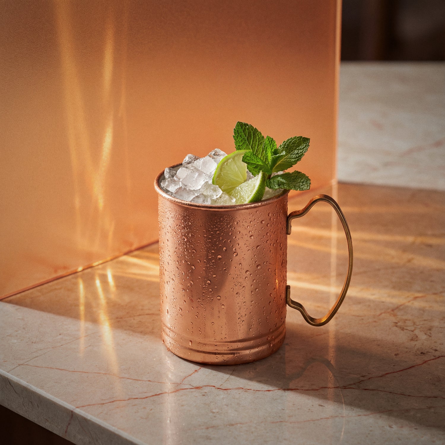Copper mug with a red orange mule cocktail garnished with lime and mint and with red orange liqueur on a marble surface.