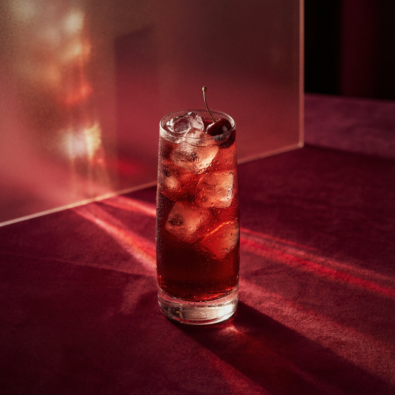 singapore sling cocktail with cherry brandy liqueur and triple sec liqueur and a cherry in a glass on a red surface