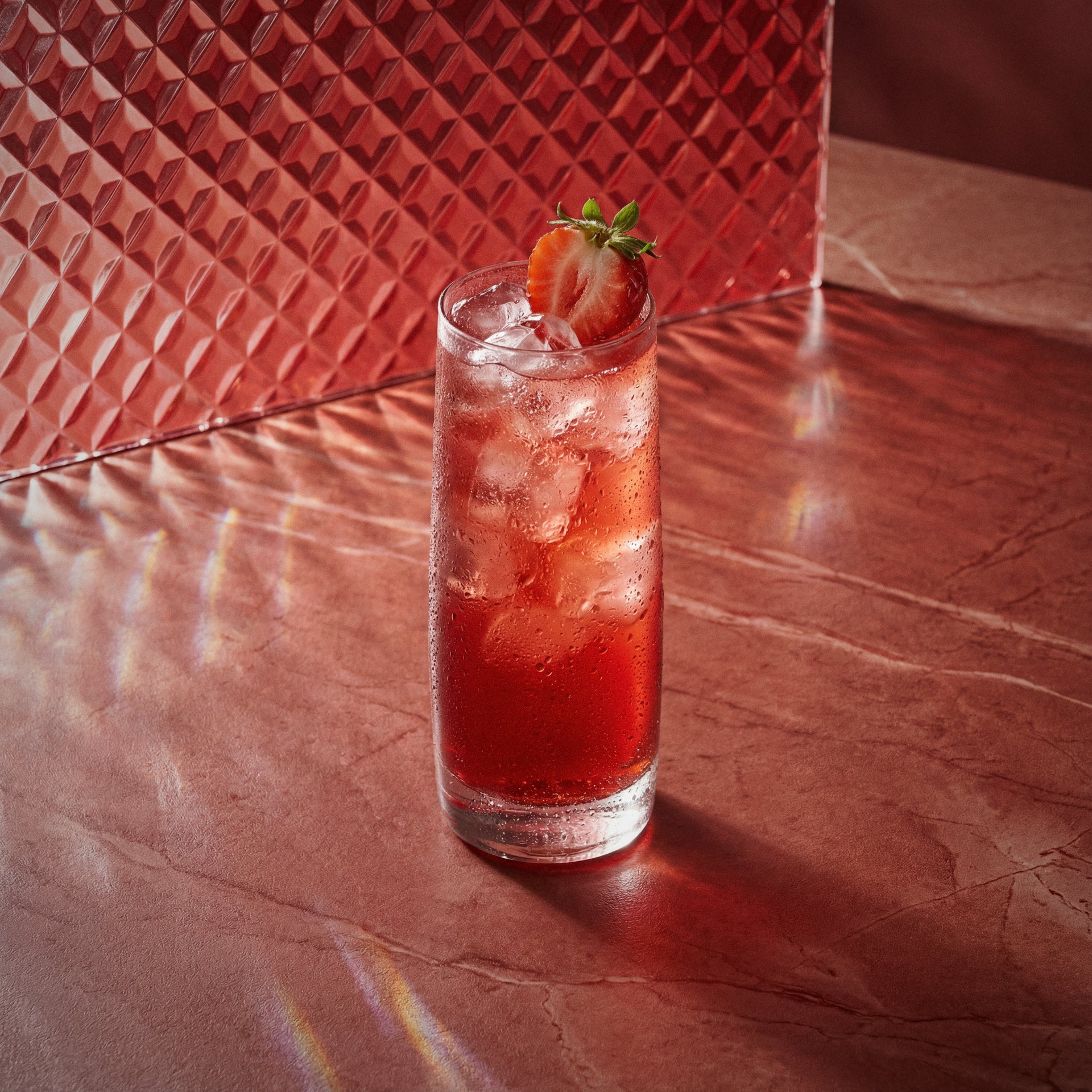 strawberry gin smash cocktail with strawberry liqueur and strawberry garnish in a highball glass and red background