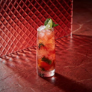 strawberry mojito cocktail with lime wedge and strawberry liqueur on a red textured surface