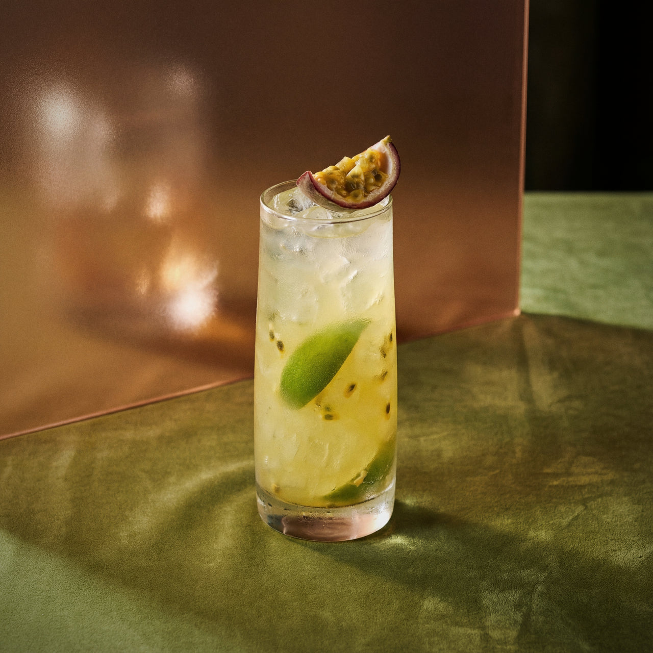 swizzle cocktail with kiwi liqueur and genever with lime and passion fruit slice on a reflective surface