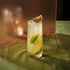 swizzle cocktail with kiwi liqueur and genever with lime and passion fruit slice on a reflective surface