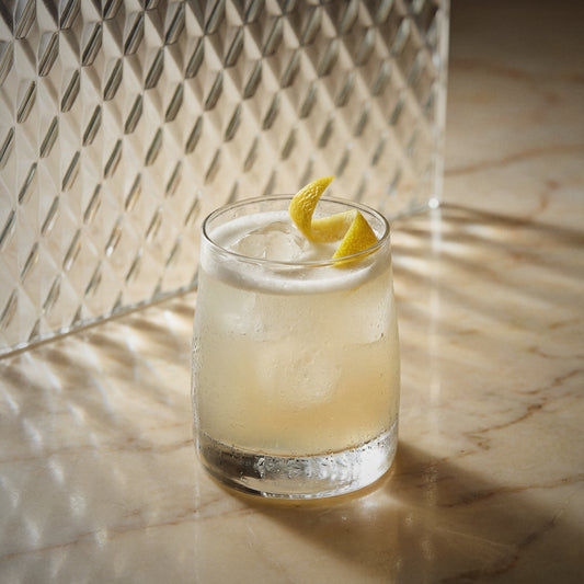 Vanilla sour cocktail with vanilla liqueur with a lemon twist on a marble surface with a textured wall background